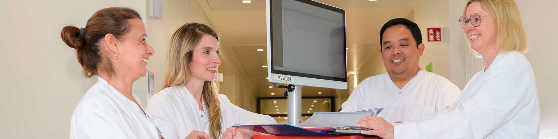 Vier Ärzte stehe im Gang am Patientenwagen und lachen sich freundlich dabei an